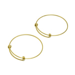 Peut inclure: Deux bracelets joncs extensibles dorés. Les bracelets sont en métal fin et ont un design simple et élégant.