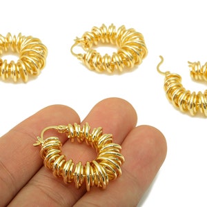 May include: Gold-colored hoop earrings with a unique coiled design. The earrings are made of a shiny, metallic material and feature a series of small, evenly spaced coils that create a textured appearance. The earrings are shown against a white background.