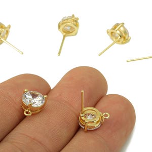 May include: Several gold-colored stud earrings with clear, round, faceted gemstones are displayed. The earrings have a classic design with a prong setting. The image shows the earrings from various angles, highlighting their sparkle and craftsmanship.