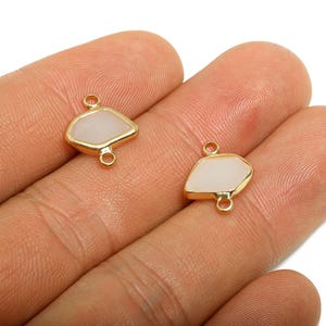 May include: Two gold-coloured, geometric-shaped jewellery connectors with a light-coloured, opaque centre. Each connector has two loops for attaching to other jewellery components. The connectors are displayed against a neutral background.