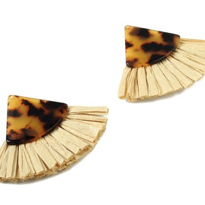 May include: A pair of earrings with a fan-shaped design. Each earring has a tortoiseshell-patterned top and a fringe of light beige material. The earrings are set against a white background, highlighting their unique design.