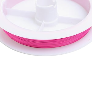 Könnte beinhalten: Eine Spule mit pinkfarbenem Garn, das um eine weiße Plastikspule gewickelt ist.