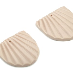 Puede incluir: Dos pendientes de color beige en forma de concha con una superficie texturizada. Los pendientes tienen un agujero en la parte superior para colgar.