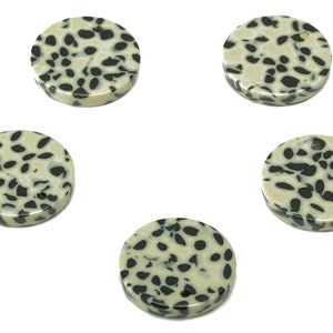 May include: Five round, flat, white and black dalmatian jasper stones. The stones have a speckled pattern of black spots on a white background.