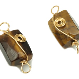 May include: Two gold wire wrapped tiger's eye pendants. Each pendant features a gold wire wrapped around the stone, creating a spiral design.