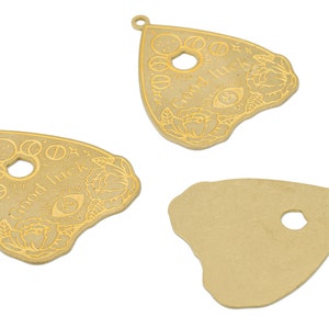 May include: Three gold-colored metal charms in the shape of a triangle with rounded edges. The charms have a hole at the top for hanging. Two of the charms have an etched design of a stylized eye, flowers, and the words "Good Luck". The third charm is plain.