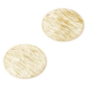 Könnte beinhalten: Zwei goldfarbene, runde Metallanhänger mit strukturierter, gebürsteter Oberfläche. Jeder Anhänger hat oben ein kleines Loch zum Auffädeln. Die Anhänger sind vor einem weißen Hintergrund platziert. Geeignet für die Schmuckherstellung.