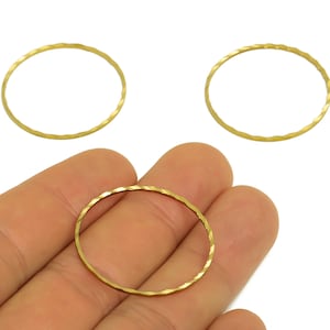 May include: Three gold-colored, hammered-finish metal circle charms. One charm is held in a hand, with two others visible in the background. The charms have a textured, faceted appearance and are suitable for jewelry making.