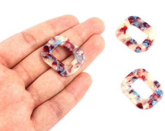 May include: Three decorative resin beads with a rectangular shape and a hole in the center. The beads have a cream base with red and blue marbled accents. One bead is held in a hand.