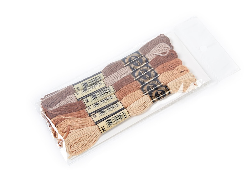 May include: A package of six spools of embroidery floss in shades of brown, beige, and tan. The spools are labeled with the brand name "A&iuml;da" and a barcode.