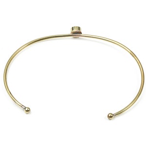 Puede incluir: Un brazalete dorado con una pequeña piedra redonda en la parte superior.