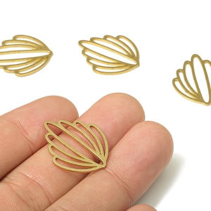 May include: Close-up of several gold-coloured, openwork shell-shaped charms. One charm is held in a hand, with three others scattered nearby. The charms have a fan-like design with multiple curved lines, set against a white background.