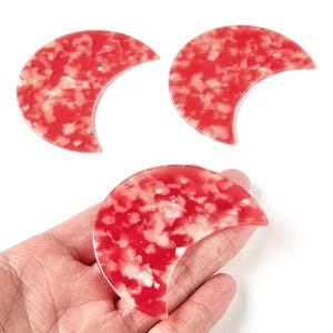 Può includere: Tre ciondoli in acrilico a forma di mezzaluna rossi e bianchi. I ciondoli hanno un motivo maculato e sono esposti su sfondo bianco. I ciondoli sono lunghi circa 5 cm.
