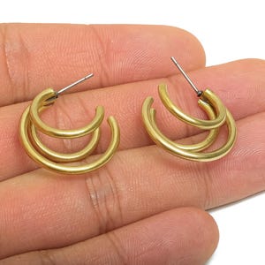 Peut inclure: Une paire de boucles d'oreilles créoles dorées. Chaque boucle d'oreille présente un design incurvé à double couche. Les boucles d'oreilles ont une tige et un fermoir pour un port sûr. Les bijoux sont présentés sur un fond neutre.