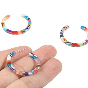 May include: A pair of colourful hoop earrings. The earrings are made of a translucent material with a mix of colours including red, blue, yellow, and purple. The earrings are round and have a post for pierced ears.