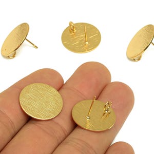 Può includere: Orecchini a bottone rotondi color oro con superficie strutturata. Gli orecchini hanno un perno e un piccolo anello per fissarli. Vengono mostrati diversi orecchini, alcuni in posizione verticale e altri angolati, su sfondo bianco.