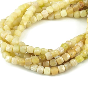 Puede incluir: Una hebra de cuentas de piedra preciosa de color amarillo claro con forma cuadrada facetada. Las cuentas están enhebradas en un hilo transparente y están dispuestas en un patrón circular.