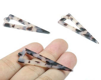 Puede incluir: Tres horquillas triangulares para el cabello con un patrón de carey. Las horquillas son de color beige claro con manchas marrones oscuras y negras. Una horquilla se sostiene en una mano. Las horquillas están hechas de un material duradero.