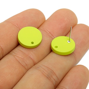 Pode incluir: Dois brincos redondos verde limão. Um brinco tem um pino de prata. Ambos os brincos têm um pequeno orifício perto da borda. Fundo neutro.