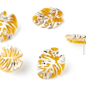 May include: A pair of yellow and white monstera leaf earrings. The earrings are made of a translucent material and have a marbled pattern.