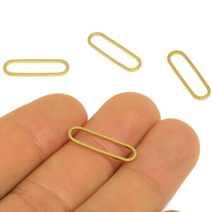May include: Close-up of several small, gold-colored oval-shaped jewelry findings. One is held in a hand, with others scattered around. These findings are likely used for jewelry making, such as earrings or necklaces.