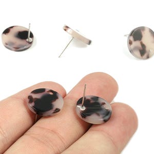 May include: Oval-shaped stud earrings with a tortoiseshell pattern in shades of brown, black, and cream. The earrings have a post backing. Several earrings are displayed on a white background.