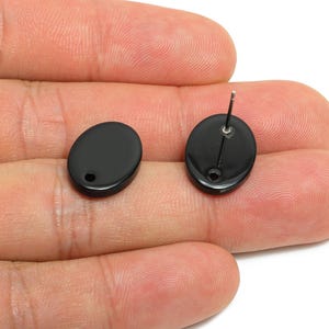 May include: Two black oval stud earrings. One earring has a post for piercing, and the other has a small hole. The earrings are smooth and glossy. The earrings are shown against a neutral background.