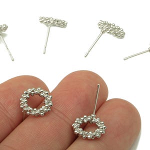May include: Silver stud earrings featuring a beaded design. The earrings are shaped as a circle and a bar. The earrings are displayed against a white backdrop.