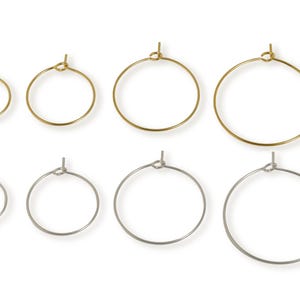 Op de afbeelding: Een assortiment gouden en zilveren oorringen in verschillende maten. De oorbellen hebben een eenvoudig, cirkelvormig ontwerp met een klein knoopdetail aan de bovenkant. De ringen zijn in twee rijen gerangschikt, met de verschillende maten.