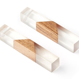 Puede incluir: Dos palos rectangulares de resina transparente con una incrustación de madera en forma de triángulo. La madera es de color marrón oscuro.