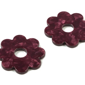 May include: Two burgundy flower-shaped decorative rings with a hole in the center. The rings have a marbled effect.