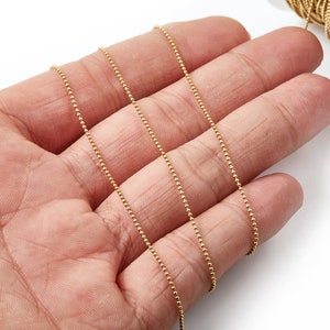 May include: A close-up of a gold chain with small round beads. The chain is lying on a hand, with the fingers spread out.