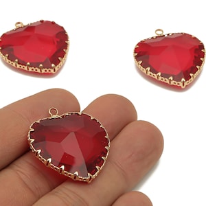 Può includere: Tre ciondoli a forma di cuore con vetro rosso sfaccettato e finiture in metallo color oro. Un ciondolo è tenuto in mano. I ciondoli hanno un anello nella parte superiore per l'infilatura. Adatto per la creazione di gioielli.