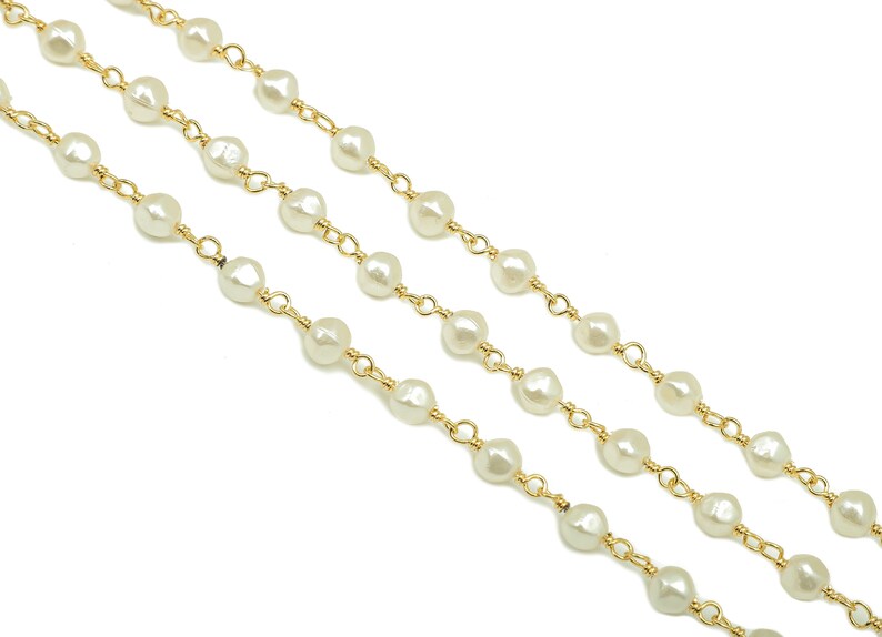 May include: A gold chain necklace with white pearl beads. The chain is made of small, delicate links.
