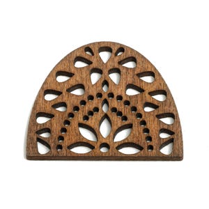May include: A wooden, semi-circular decorative element with a floral design. The dark brown piece features cut-out shapes, including teardrops and circles, creating an openwork pattern. The item is set against a white background.