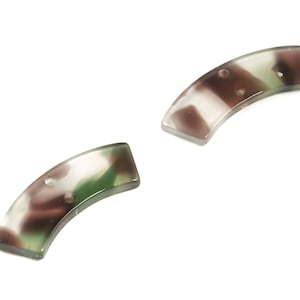 Może przedstawiać: Dwa plastikowe spinki do włosów w kamuflażu. Spinki są zakrzywione i mają przezroczystą, białą podstawę z brązowymi i zielonymi wirami.