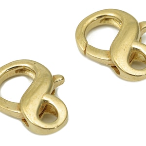 Puede incluir: Dos cierres de langosta de metal dorado, cada uno con una forma redonda y lisa. Los cierres están diseñados para usarse para sujetar joyas u otros artículos.