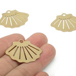 Può includere: Tre ciondoli a forma di conchiglia color oro. Ogni ciondolo ha un bordo smerlato e una serie di ritagli verticali, che ricordano la forma di una conchiglia. I ciondoli hanno un piccolo anello nella parte superiore per il fissaggio.