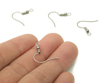 May include: Silver-colored earring hooks with a curved wire and a small ball and coil design. Several hooks are scattered on a white background, with one hook held in a hand.