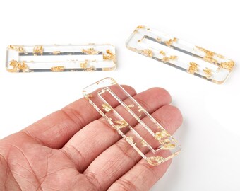 Puede incluir: Horquillas rectangulares transparentes de resina con inclusiones de pan de oro. Una horquilla se sostiene en una mano, con otras dos cerca. Las horquillas tienen un recorte rectangular en el centro.