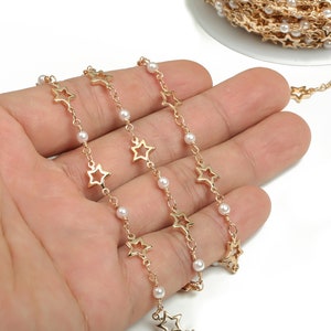 May include: Gold chain with star-shaped links and white pearl beads. The chain is coiled on a hand.