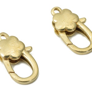 Puede incluir: Dos cierres de metal dorado con un diseño de trébol. Cada cierre tiene una abertura de resorte y un bucle para sujetarlo a una cadena o cordón.