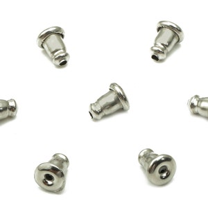 May include: Seven silver earring backs, also known as earring stoppers, are arranged in a circle on a white background.