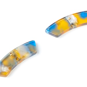 May include: Two blue, yellow and white marbled plastic buttons. The buttons are shaped like a curved rectangle.