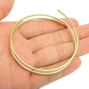 Könnte beinhalten: Ein gewickeltes, goldfarbenes Drahtarmband, das in einer Hand gehalten wird. Das Armband besteht aus dünnem, rundem Draht und hat ein schlichtes, elegantes Design. Das Armband hat einen Durchmesser von ca. 7.6 cm.