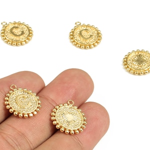 May include: Gold-colored metal charms with the letter "C" in a decorative font. The charms have a circular shape with a beaded border and a small loop for attaching to jewelry. The charms are shown against a white background.