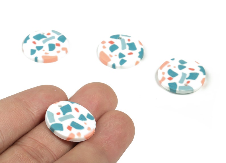 May include: Four round, white ceramic pendants with a terrazzo pattern in shades of teal, pink, and white.