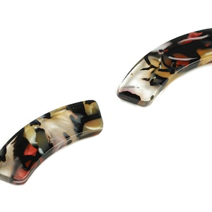 Może przedstawiać: Dwa brązowe, czarne i białe wzorzyste spinki do włosów. Spinki są zakrzywione i mają błyszczące wykończenie.