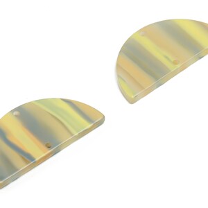 Może przedstawiać: Dwa półkoliste elementy z żywicy z marmurowym wzorem w odcieniach żółtego, pomarańczowego i szarego. Każdy element ma dwa otwory do nawlekania.