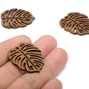 May include: Three brown wooden leaves with a cutout design resembling a monstera leaf. The leaves are approximately 2 inches in length.
